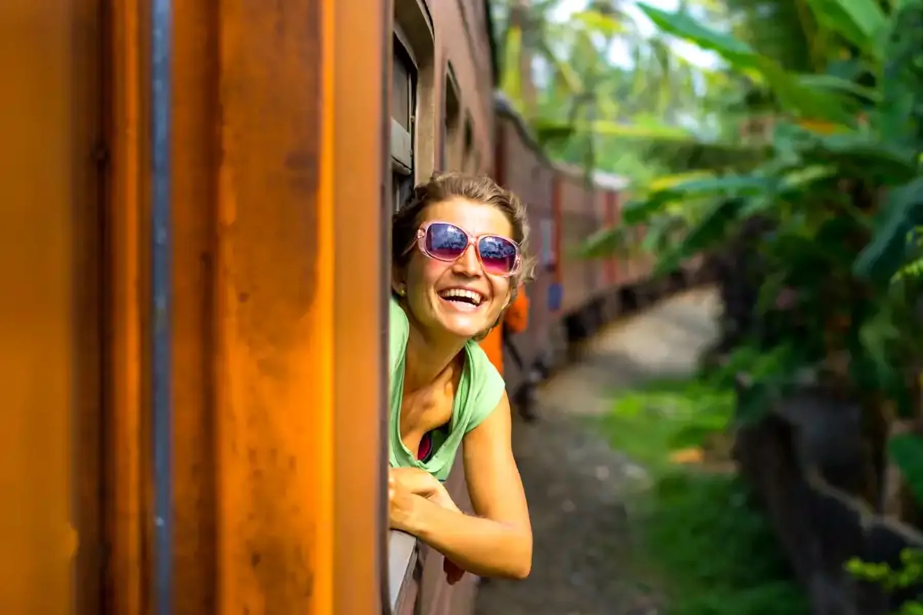 Une voyageuse souriante se penche à la fenêtre d’un train
